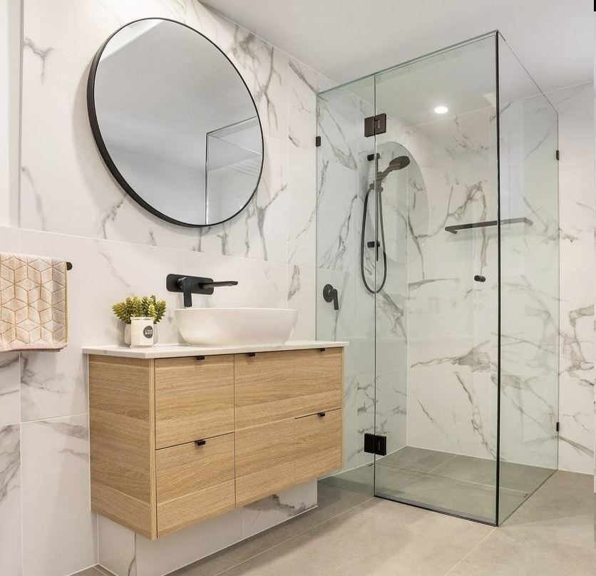 Frameless corner shower screen with black hinges in a marble-tiled bathroom